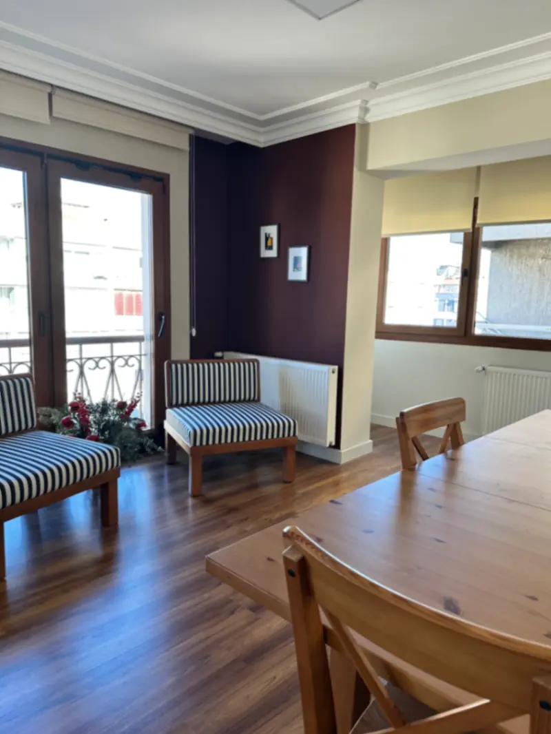 Balkona açılan bekleme alanı, çizgili oturma bankları ve ahşap masa — çocuk ve genç psikiyatristi muayenehanesi, İzmir Alsancak
